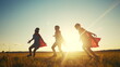 © maxximmm - team superhero. a group of children are running across the field in a superhero costume with a silhouette of a red cape at sunset. the concept teamwork of a happy family childhood. superhero dream