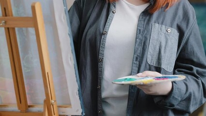 Wall Mural - Close-up female hands of unrecognizable woman artist painter girl art college student holding palette with oil acrylic paints using paintbrush for drawing painting draws picture on canvas on easel