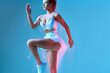 © Georgii - Amazing fitness woman bouncing on blue background. Studio portrait of brunette lady with a pony tale.