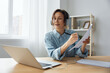 © SHOTPRIME STUDIO - Attentive smiling happy female student in headphones learning from online lectures at home writes down synopsis on sheet. Happy office employee is at video conference using laptop. Copy space