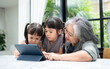 © Prot - Asian Grandmother with her two grandchildren having fun and playing education games online with a digital tablet at home in the living room. Concept of online education and caring from parents.