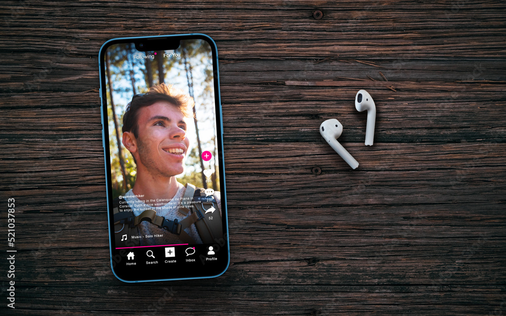 Sample social media app interface on mobile phone on a wooden table with headphones, concept of modern networking and sharing of short form video content