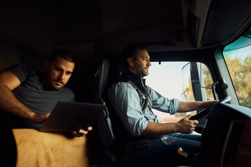 Wall Mural - Professional driver driving truck while his colleague is using laptop in cabin.