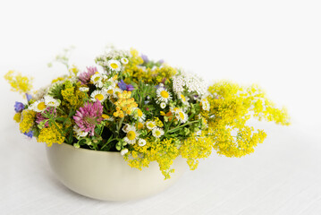 Poster - Summer blooming delicate flowers in a round vase on a table with a white tablecloth, a pastel bouquet and a delicate floral card