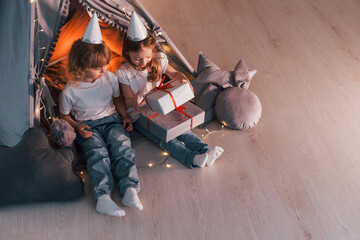 Wall Mural - Holiday surprise. With gift boxes. Two little girls is in the tent in domestic room together