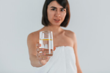 Wall Mural - Holding glass with water. Young brunette is indoors against white background