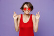 © ViDi Studio - Young fun woman 20s she wear red tank shirt eyeglasses waiting for special moment, keeping fingers crossed, making wish, eyes closed isolated on plain purple backround studio People lifestyle concept
