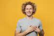 Young smiling kind-hearted happy fun cheerful caucasian man 20s he wear grey t-shirt look camera put folded hands on heart isolated on plain yellow backround studio portrait. People lifestyle concept.