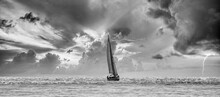Black And White View Of A Sailboat Navigating A Silvery Sea In A Stormy Cloudy Sunset