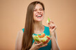© Yuriy Shevtsov - Happy laughing lady with closed eyes in azure dress eating green salad from glass bowl, isolated portrait on peach color background