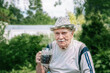 © oksanamedvedeva - large portrait of a gray-haired old man in a hat with a glass of dark drink. man with a glass mug is sitting in the garden.