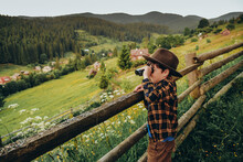 A Boy Looks Through Binoculars While Standing On A Hilltop In Summer. Family Trip To The Mountains In Summer.