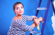 © lenets_tan - Beautiful young woman doing wall painting, standing on ladder. Beautiful young woman