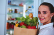 © lenets_tan - Young woman holding grocery shopping bag with vegetables .Standing in the kitchen