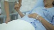 © DG PhotoStock - Asian young woman taking care of her mother who resting on the bed in hospital ward. Young woman talking to elder woman.