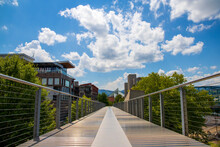 A Long Gray Metal Bridge Surrounded By Red And Brown Buildings And Lush Green Trees And Plants With Mountains And Blue Sky With Clouds In Chattanooga Tennessee USA