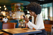 © fotofabrika - Young afro woman using mobile phone at coffee shop