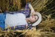 © olga_sova - A beautiful middle-aged farmer woman in a straw hat and a plaid shirt stands in a field of golden ripening wheat during the daytime in the sunlight