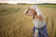 © olga_sova - A beautiful middle-aged farmer woman in a straw hat and a plaid shirt stands in a field of golden ripening wheat during the daytime in the sunlight