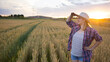 © olga_sova - A beautiful middle-aged farmer woman in a straw hat and a plaid shirt stands in a field of golden ripening wheat during the daytime in the sunlight