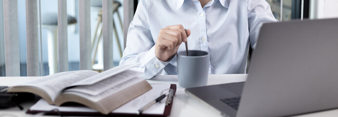 Canvas Print - Businesswoman working on laptop and sipping coffee comfortably, Sitting in a private office, Using computers to conduct financial transactions, World of technology and internet, Work lifestyle.