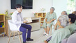 © tampatra - An Asian doctor talking to a group of old elderly patient or pensioner people smiling, relaxing, having fun together in nursing home. Senior lifestyle activity recreation. Retirement. Health care
