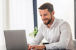 © kucherav - Successful businessman working using computer laptop sitting at the workplace in modern office. Bearded man entrepreneur in white shirt typing on keyboard, smiling