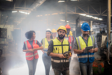 Wall Mural - group of diversity teamwork, engineers, technician and workers team in safety uniform workwear having discussion while walking through machinery and smoke in heavy industry manufacturing factory.
