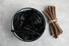 Tasty Black Candies And Dried Sticks Of Liquorice Root On Grey Table, Flat Lay