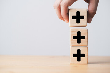 Hand stacking plus sign which print screen on wooden cube block for addition and positive mindset thinking concept.