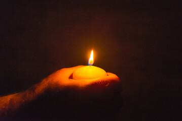 Wall Mural - Burning candle in a mans hand religion concept.Candle in hands on a dark background.