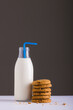 Milk bottle with straw by stack of cookies against gray background, copy space