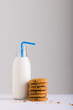 Milk bottle with straw by stack of cookies against white background, copy space