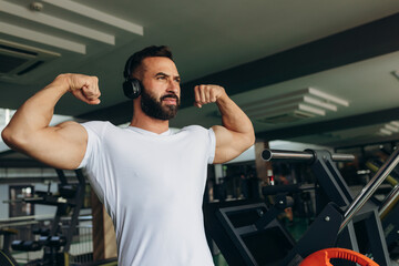 smiling sports man in white t-shirt showing his muscles in the gym