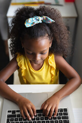 Wall Mural - High angle view of african american elementary schoolgirl using laptop at desk in classroom