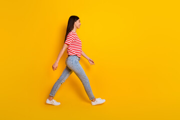 Full length profile portrait of pretty cheerful person walking look empty space isolated on yellow color background