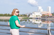 © Alena - A view from the back of a girl in a green blouse standing on the riverbank against the background of a blurred city. A girl walks through the streets of the city.