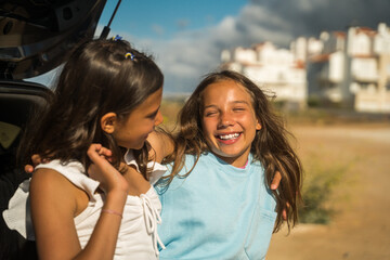 Wall Mural - Smiling little sisters embracing and chatting while spending time together near the car