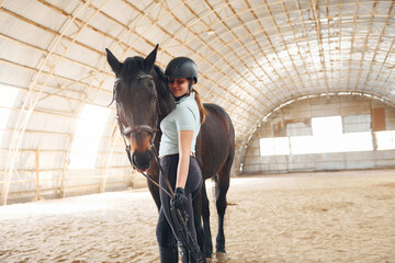 Wall Mural - At daytime. A young woman in jockey clothes is preparing for a ride with a horse on a stable