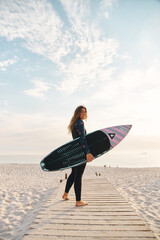 Extreme Sports Female Adventurer At The Beach Walking Down Jetty With Surf Board Or Kite Surfing In Wetsuit