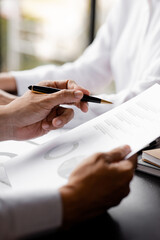  A close-up view of a businessman holding a pen pointing at a bar chart on a company financial document prepared by the Finance Department for a meeting with business partners. Financial concept.