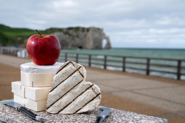 Cheeses of Normandy, round camembert cow cheese from Calvados region and heartshaped neufchatel from Neufchâtel-en-Bray and view on alebaster cliffs Porte d'Aval in Etretat, Normandy, France