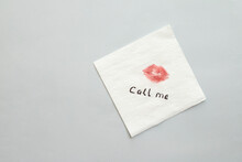 Paper Napkin With Lipstick Mark And Words CALL ME On Grey Background, Top View. Space For Text