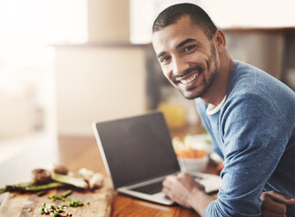 Aufkleber - Young man on a laptop while preparing a healthy meal at home. Portrait Happy smiling male browsing and learning on computer in the kitchen on how to cook. Guy alone checking online recipes on the web