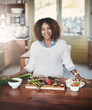 Portrait of happy black woman preparing healthy food in a kitchen at home. Young African American using fresh vegetables to make a delicious, balanced low carb meal. Lady on a cleanse and detox diet
