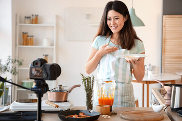 Canvas Print - Young Asian woman holding plate with pumpkin soup while recording video class in kitchen