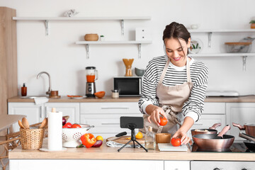 Sticker - Young woman with fresh tomatoes following cooking video tutorial in kitchen