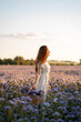 © Анжелла Антоновская - A beautiful girl with a basket walks through a field with purple flowers at sunset