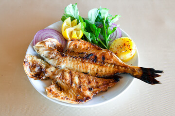 Grilled sea bass ( Levrek Izgara ) served on a plate with various sauces and decorated with parsley and lemon