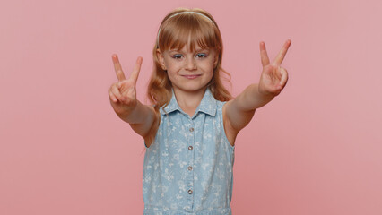 Wall Mural - Happy preteen child girl kid showing victory sign, hoping for success and win, doing peace gesture smiling with kind optimistic expression. Little toddler children isolated on studio pink background